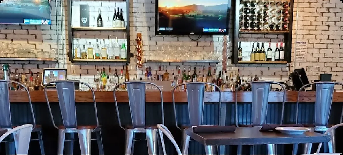 Bar interior with metal stools, white brick wall, bottle shelves