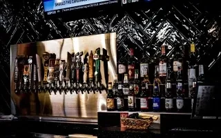 A dimly lit bar with numerous beer taps and illuminated spirit bottles.