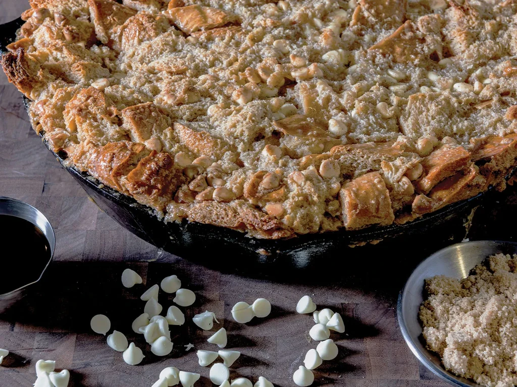 Rustic golden-brown dessert in skillet, with sauce, sugar, chocolate chips.