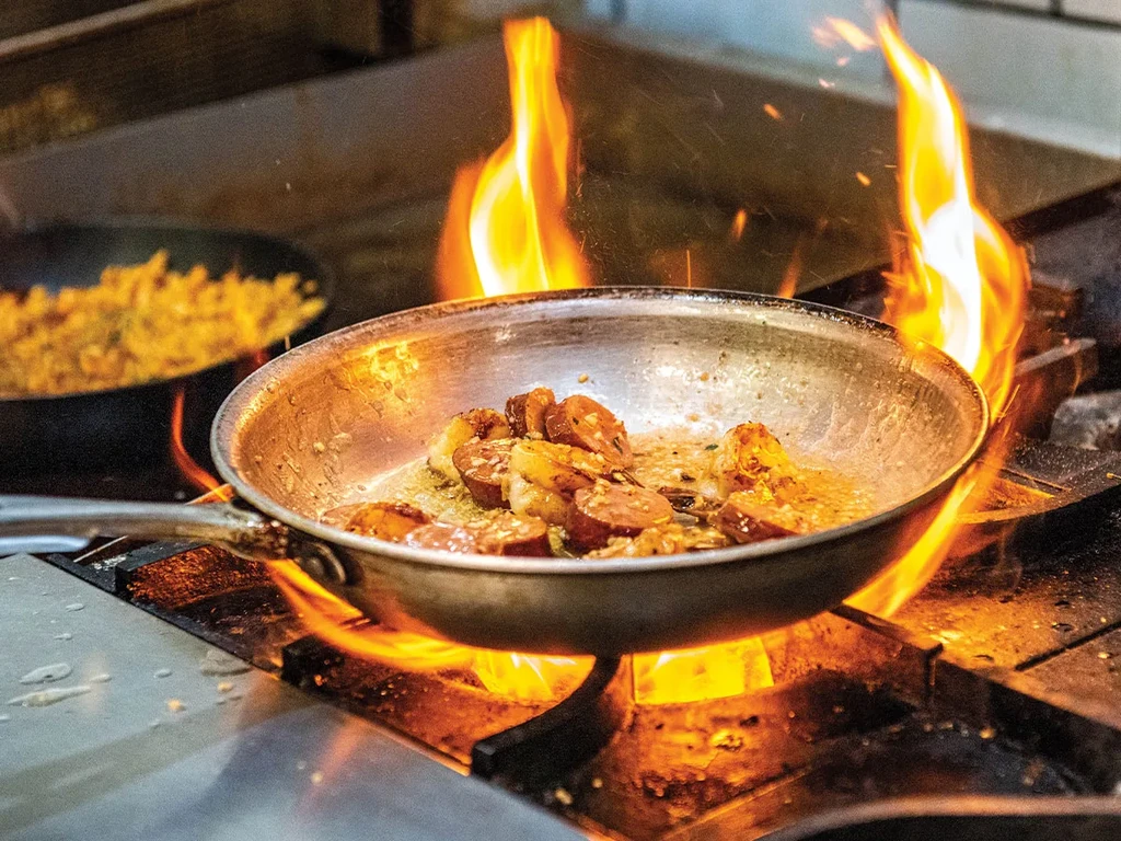Sauté pan intensely flaming on a stovetop with food cooking.