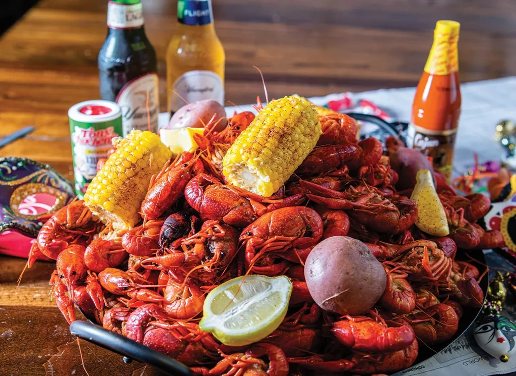 Close-up of seasoned crawfish boil with corn, potatoes, and Mardi Gras decor.