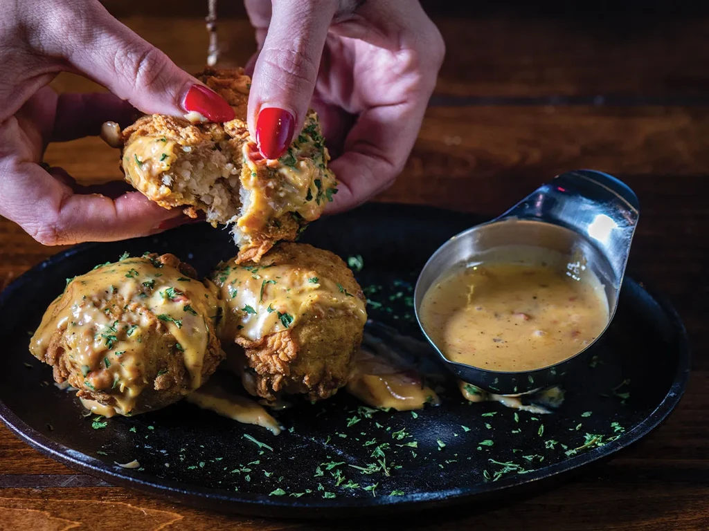 Hands pull apart a fried item with golden sauce and green herbs.