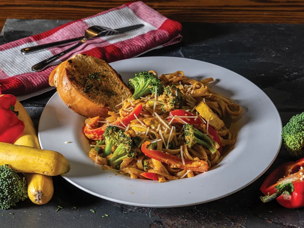 Plate of pasta with vegetables, garlic bread, and raw produce.