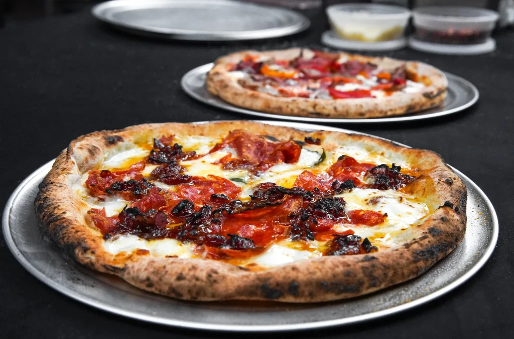 Artisanal Neapolitan pizzas on trays, topped with cheese, pepperoni, vegetables.