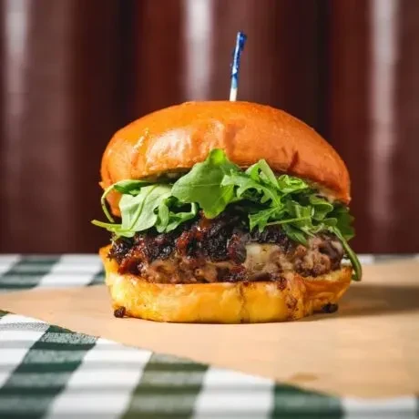 Gourmet burger with brioche bun, patty, cheese, onions, and arugula.
