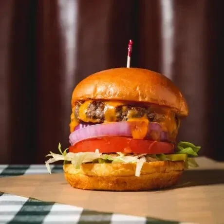 A close-up double cheeseburger with melted cheese, onion, tomato, lettuce.