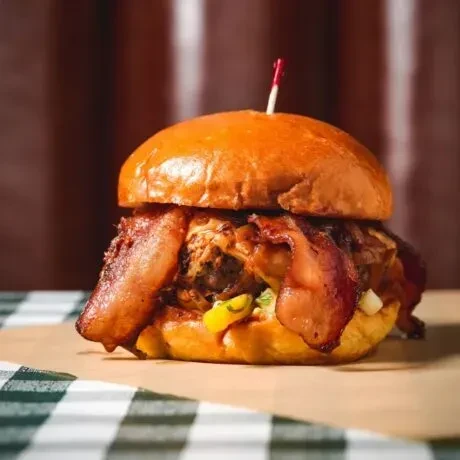 Close-up gourmet burger with crispy bacon, melted cheese, and green onions.