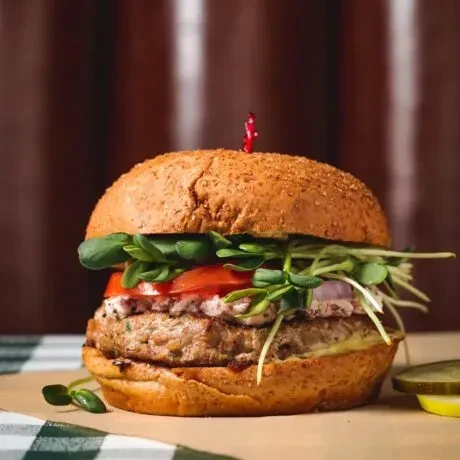 Chicken burger with sprouts, tomatoes, onions, and pickles on checkered cloth.