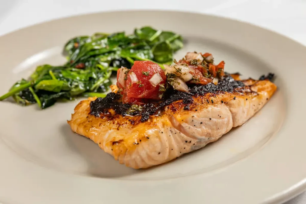 Grilled salmon fillet with tomato salsa and sautéed spinach on a plate.