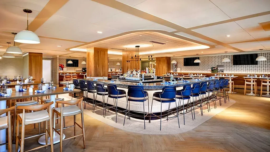 Well-lit modern bar and restaurant interior with blue stools and houndstooth walls.