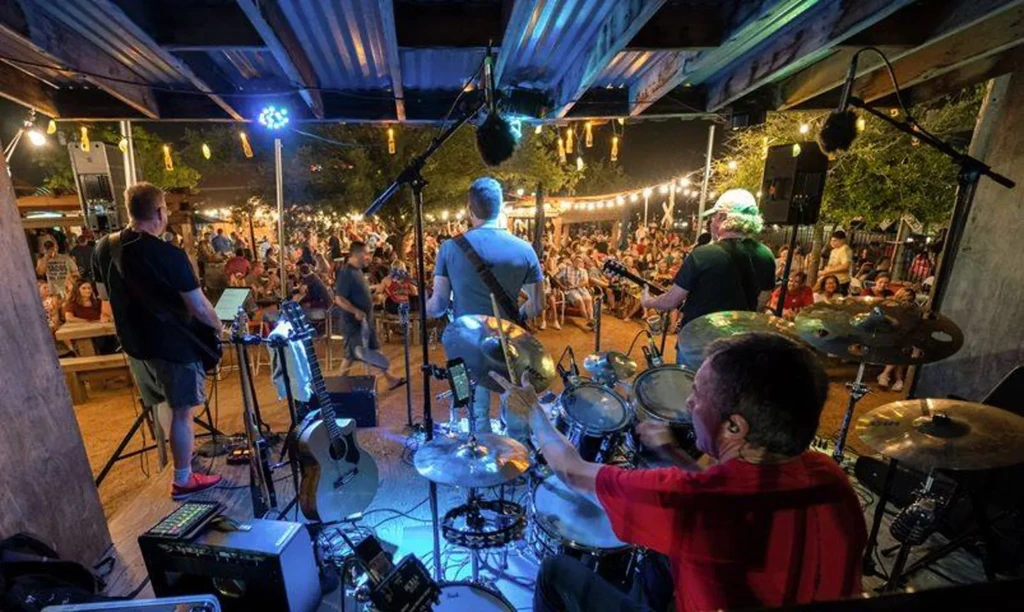 Live band performing outdoors at night with stage and string lights.