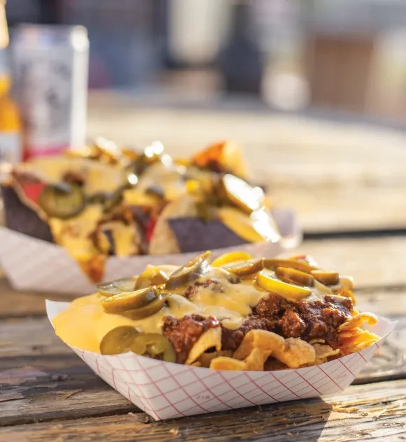 Two trays of chili cheese nachos with jalapeños on a rustic table.