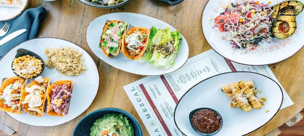 Overhead view of a wooden table with various Mexican and Latin dishes.