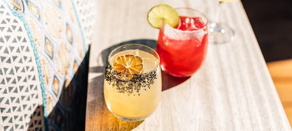 Two vibrant cocktails: yellow with dried citrus, red with fresh lime.