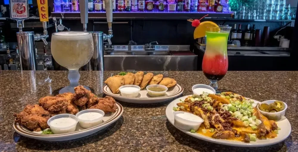 Vibrant bar counter displaying fried food, beer, and colorful cocktails.