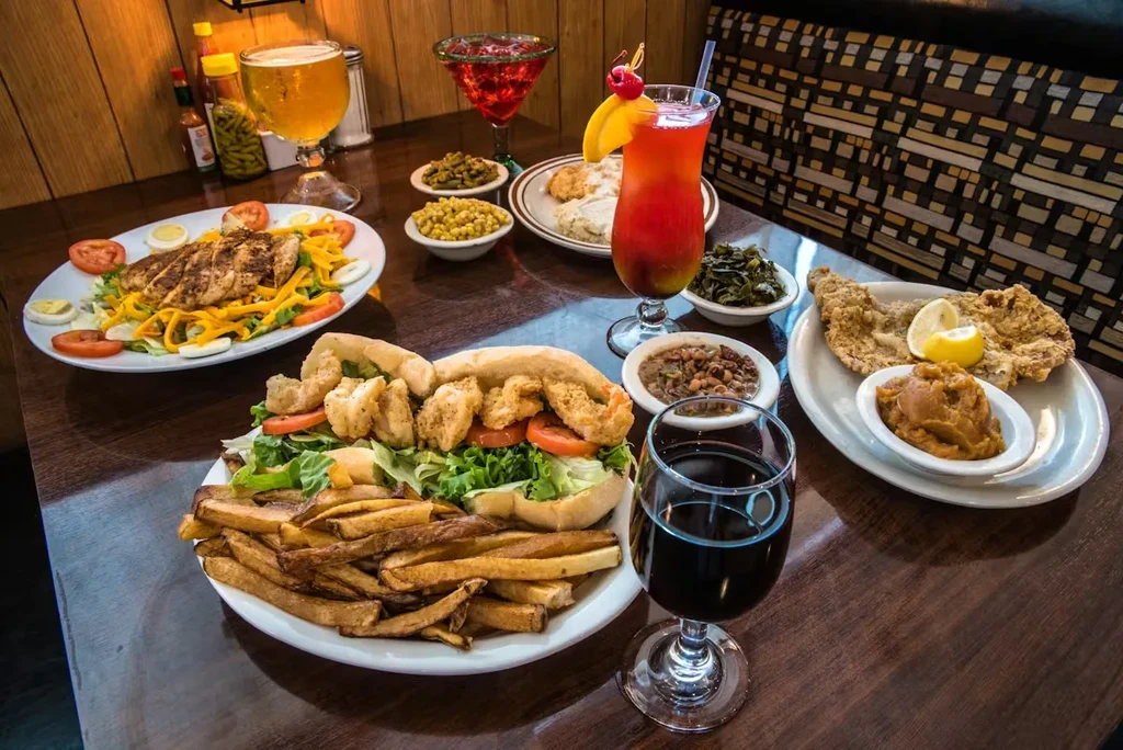 Restaurant table with shrimp po'boy, fried fish, chicken salad, and drinks.