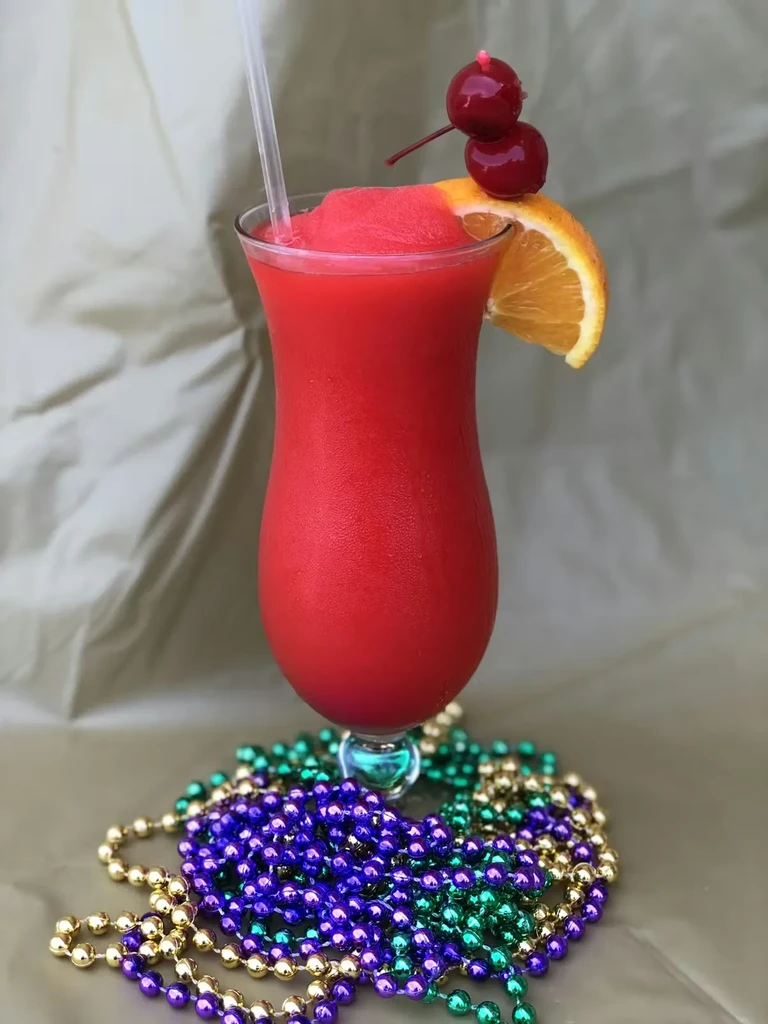 Red frozen cocktail, orange, cherries, and colorful Mardi Gras beads.