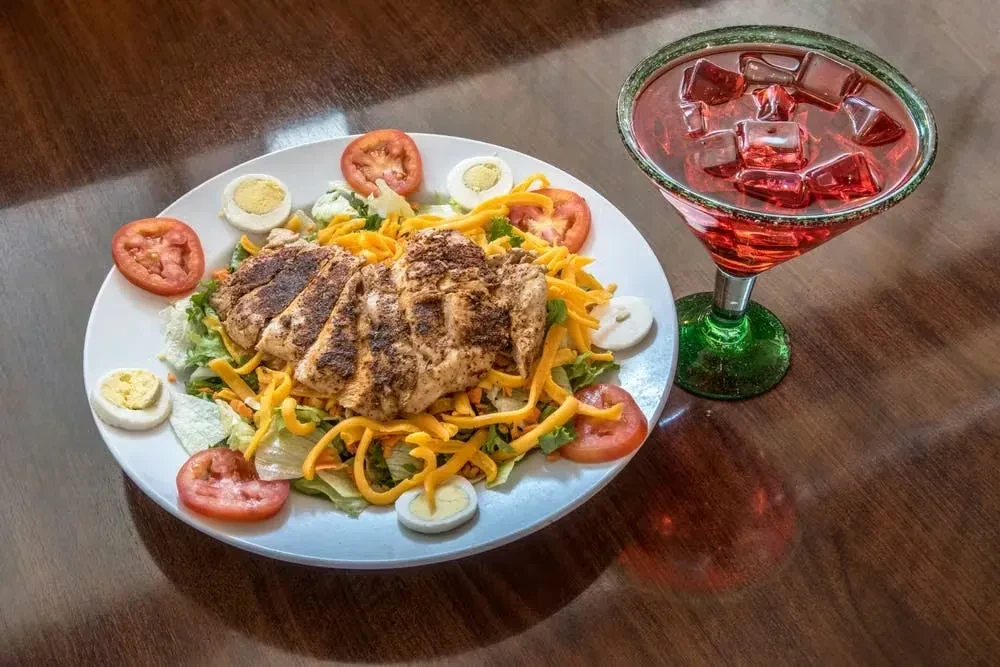 Grilled chicken salad, hard-boiled eggs, red drink in margarita glass, on table.