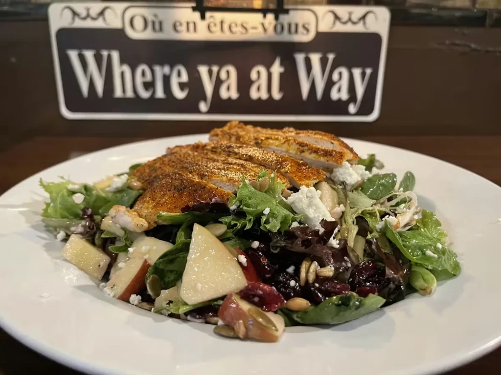 Plated grilled chicken salad with apples, cranberries, seeds, and feta.