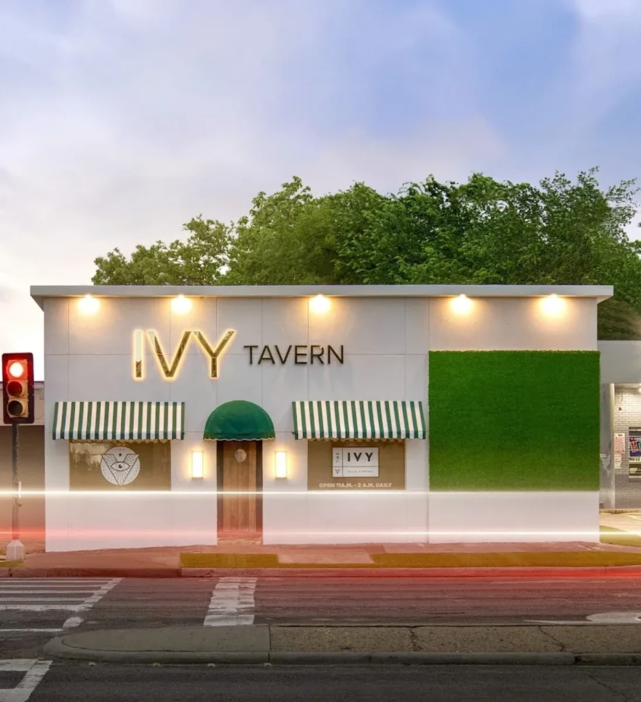 Illuminated Ivy Tavern exterior at night, with white facade and green wall.