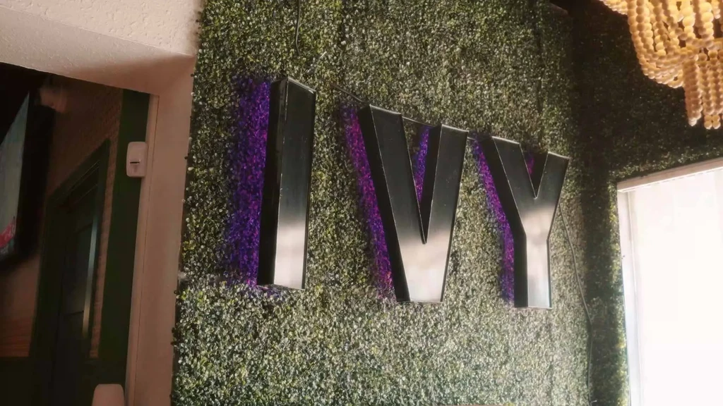 Purple-backlit "IVY" letters on a wall of artificial greenery.