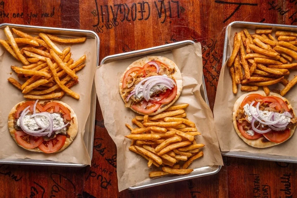Three pita meals with meat, vegetables, white sauce, and french fries.