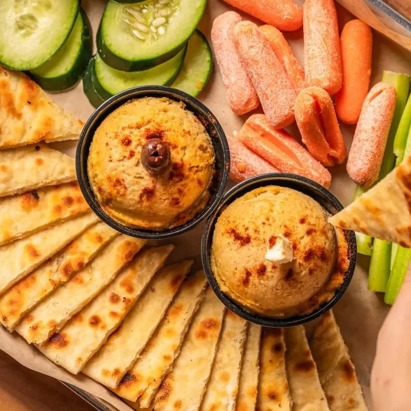 Overhead view: Hand dips pita into hummus on colorful appetizer platter.