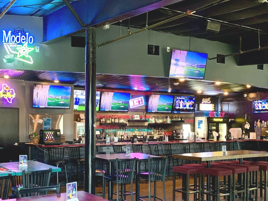 Empty sports bar with a stocked bar, TVs, and neon signs.