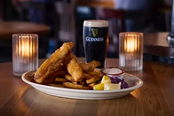 Close-up: Golden fish and chips, Guinness pint, lemon, tartar sauce in pub.