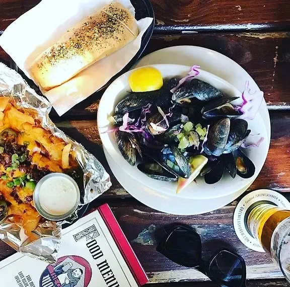 Mussels, loaded fries, bread, and beer on a rustic wooden table.