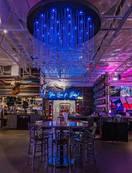 Bar interior with blue chandelier, neon sign, and rustic decor.