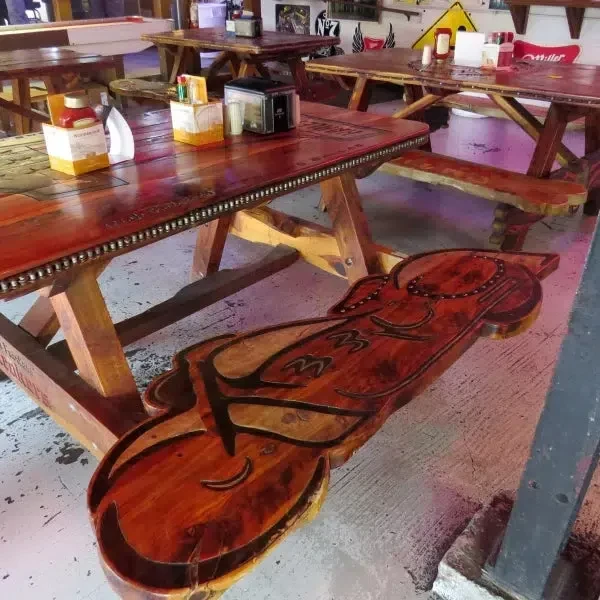 Restaurant interior with rustic wooden tables and a carved instrument bench.