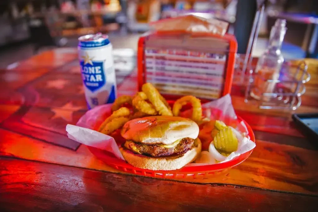 Cheeseburger, onion rings, pickles, and Lone Star beer in red basket.