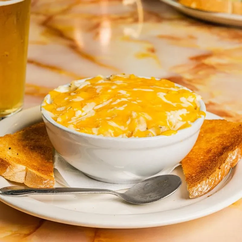 White bowl of creamy dish with melted cheese and toasted bread.