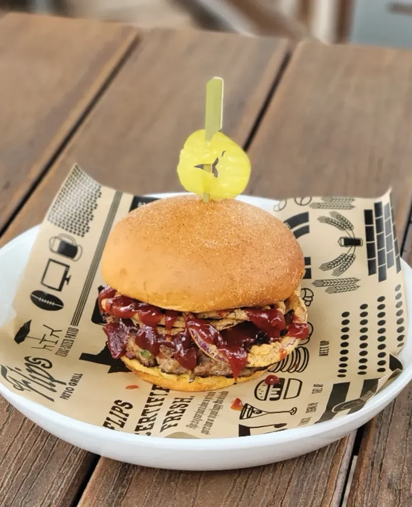 Close-up of a burger with BBQ sauce and skewer on branded paper.