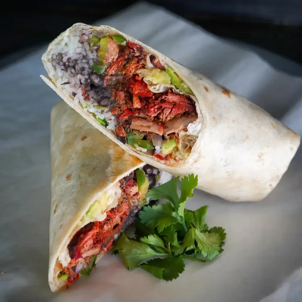 Large burrito cut diagonally, showing rice, beans, red meat, avocado, cilantro.
