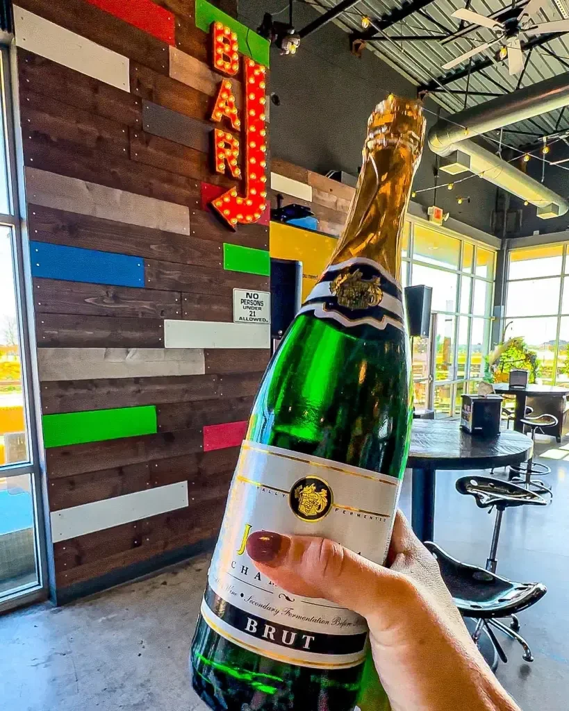 Hand holding a green champagne bottle in a trendy bar setting.