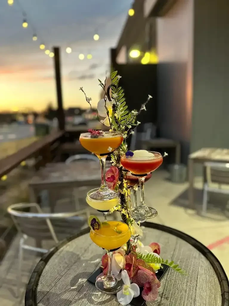 Four vibrant cocktails on a multi-tiered floral display at sunset.