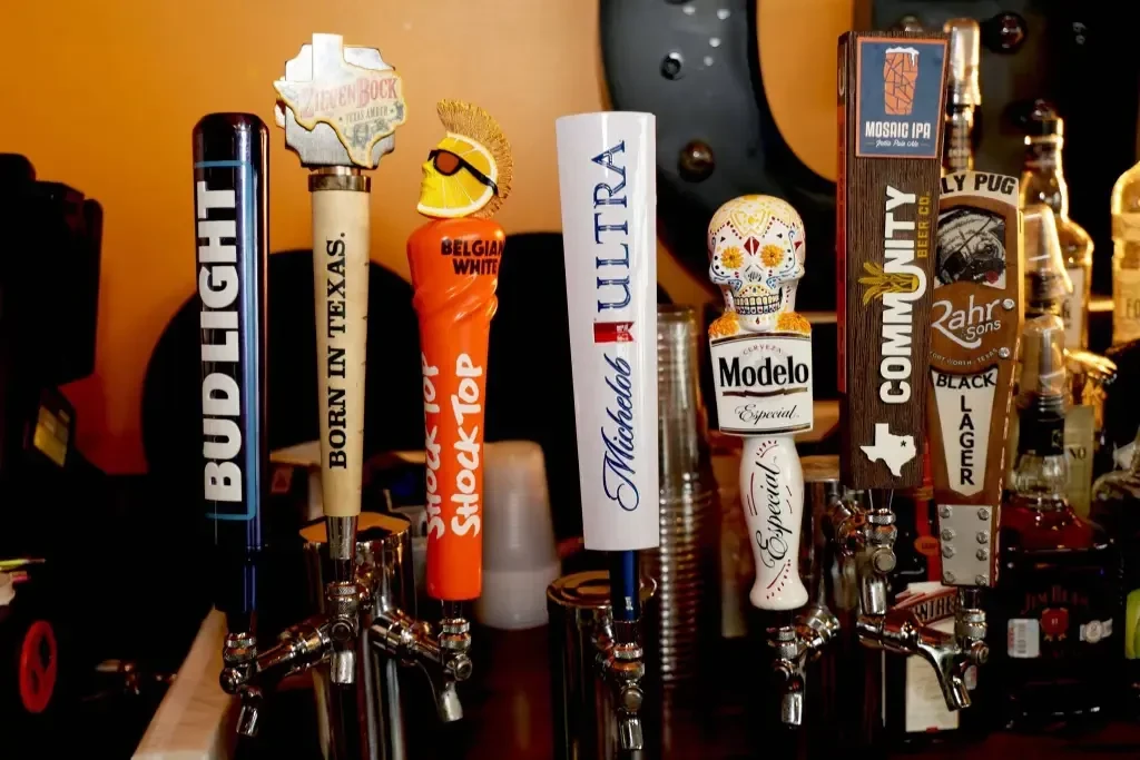 Close-up of diverse branded beer tap handles on shiny chrome faucets.