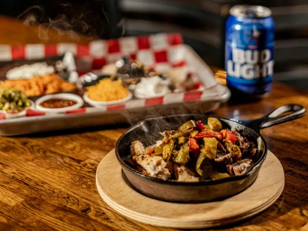 Sizzling chicken and beef fajitas in a skillet with sides and a beer.