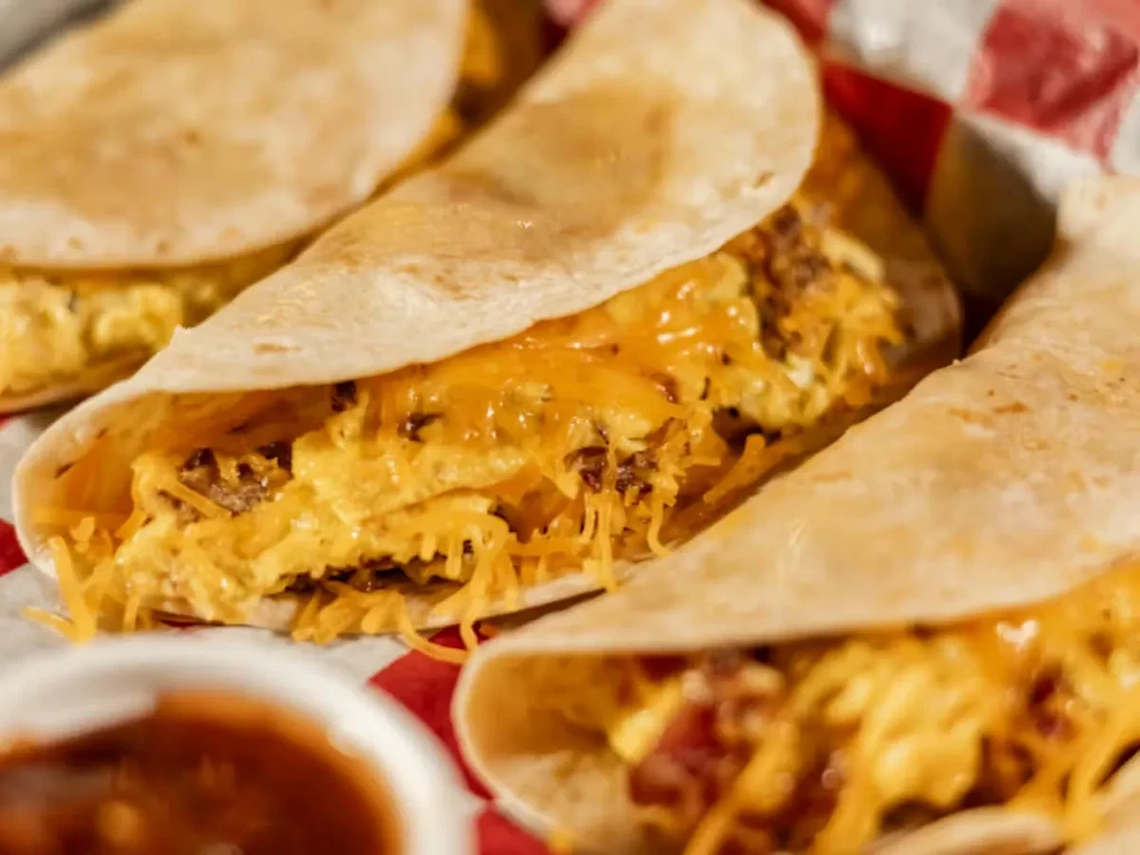 Three soft tacos with eggs, cheese, and meat on a checkered liner.