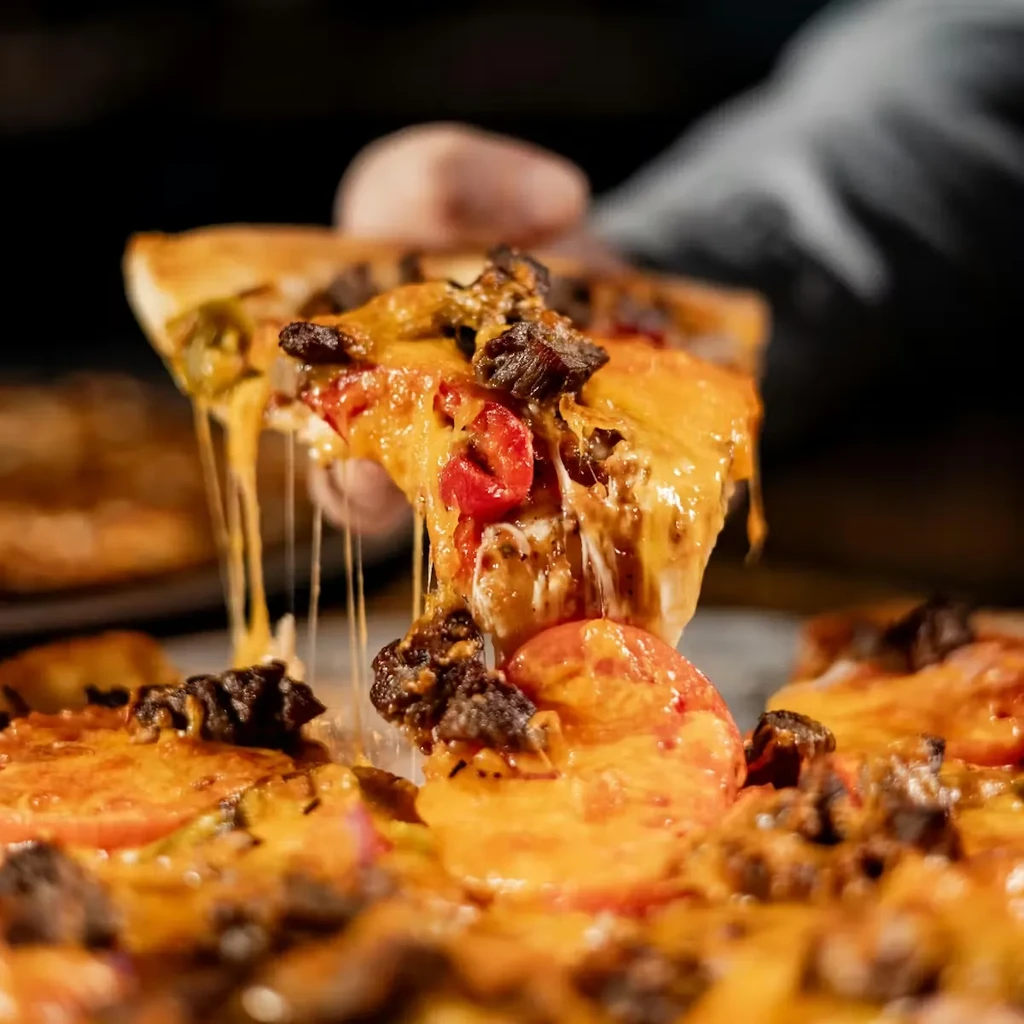 Lifted pizza slice with stretching melted cheese, tomatoes, meat, golden crust.