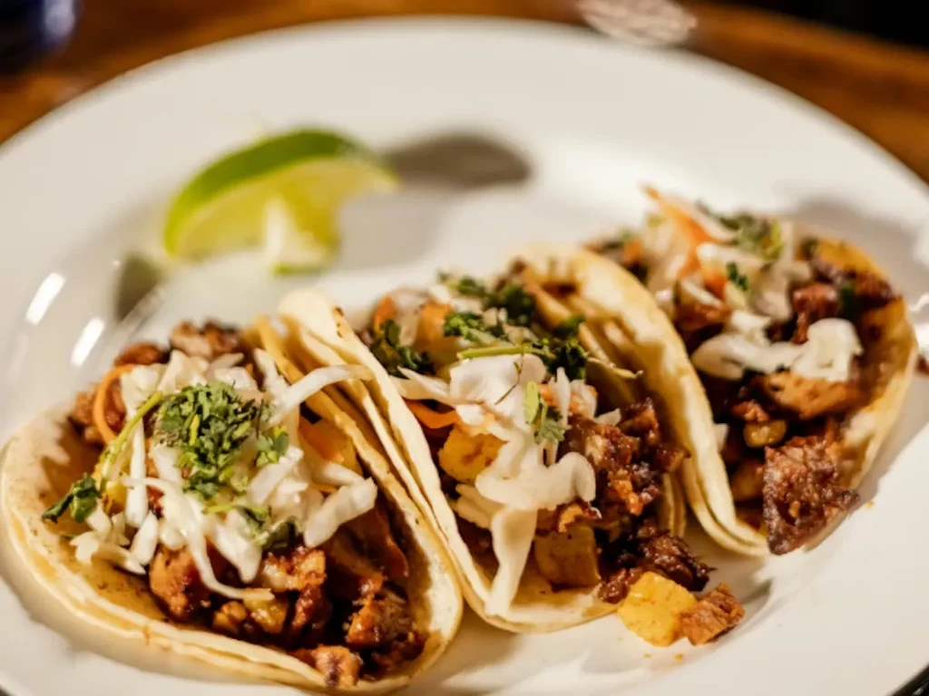 Three street-style tacos with meat, slaw, cilantro, and lime.