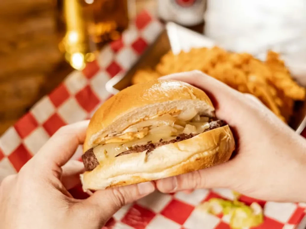 Close-up of hands holding a classic cheeseburger on checkered paper.