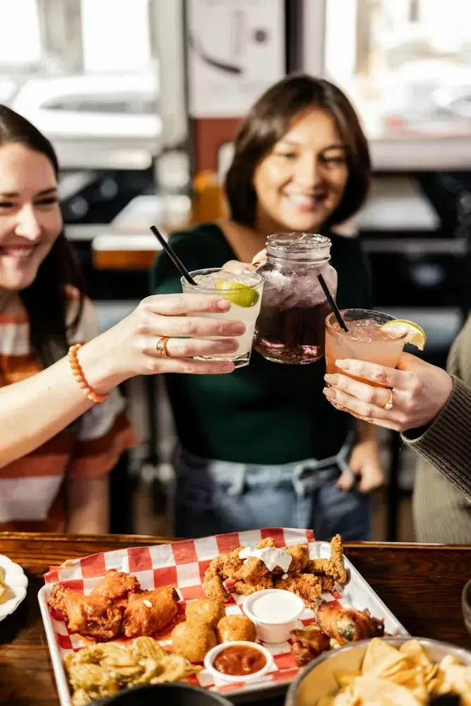 Three people toasting drinks over a platter of fried appetizers.