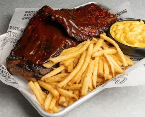 Barbecued ribs, golden fries, and creamy mac and cheese on a tray.
