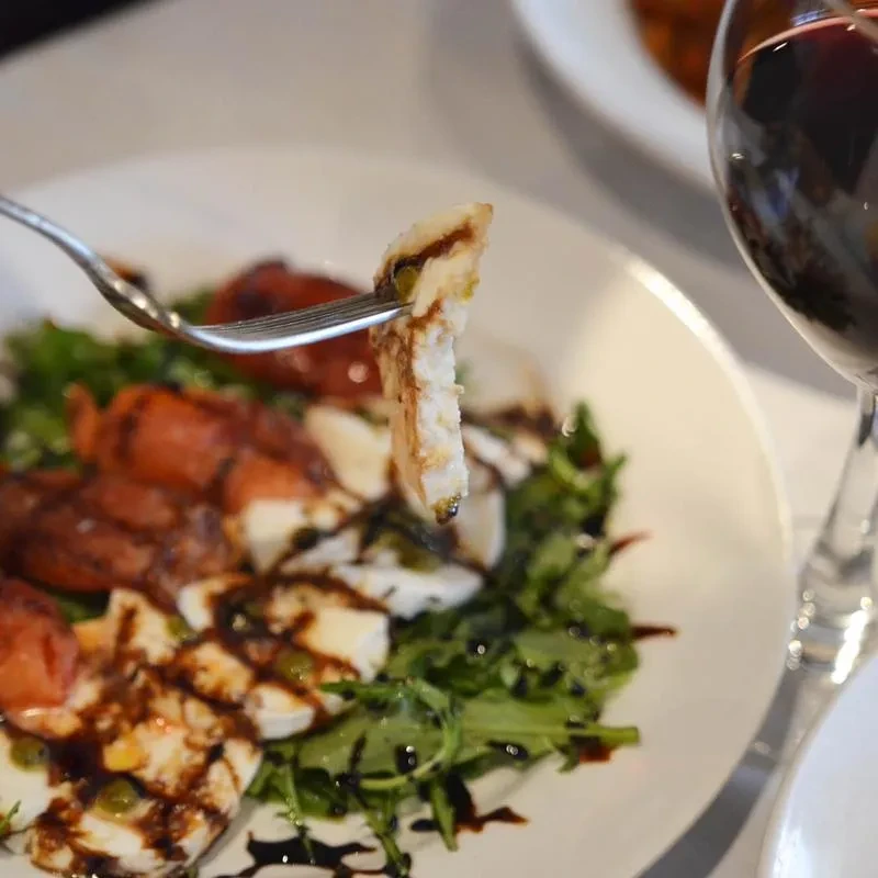 Restaurant salad: fork lifting grilled chicken, mozzarella, tomatoes, balsamic.