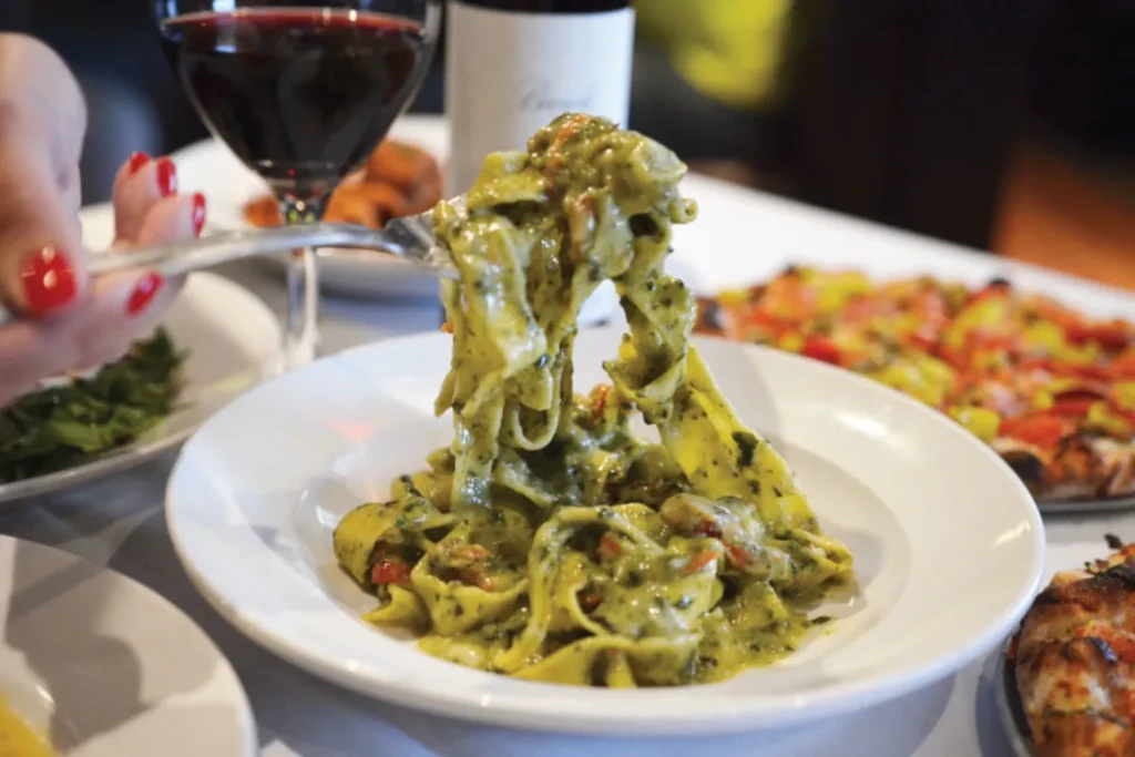 Fork lifting vibrant green pesto pasta from a white plate.