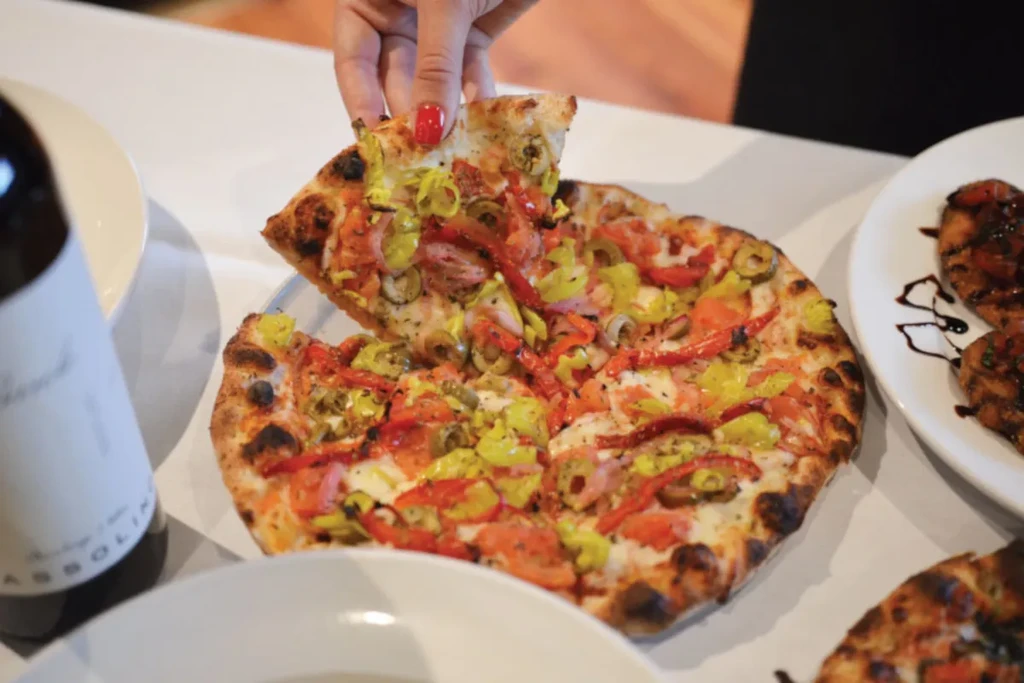 Gourmet pizza with cheese, tomato, peppers, olives; hand lifts slice.