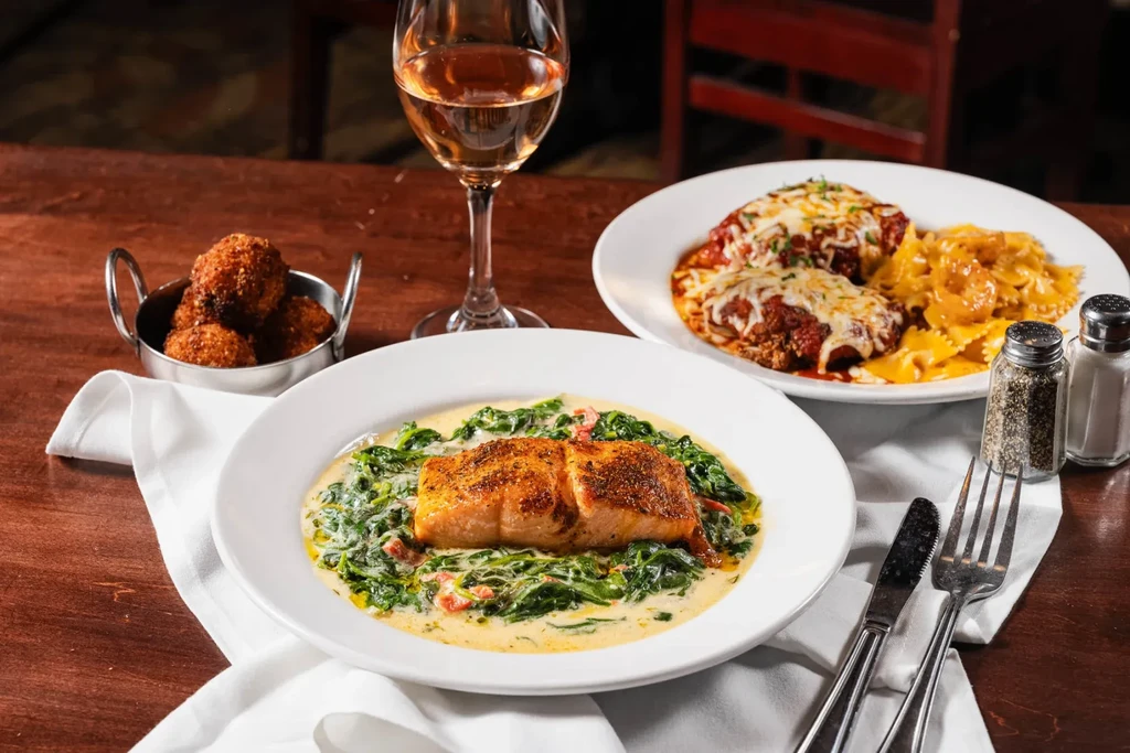 Seared salmon, chicken parmesan, pasta, and appetizers on a restaurant table.